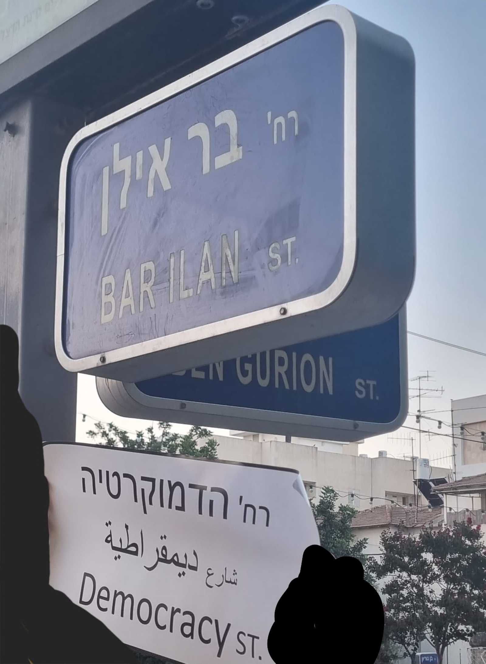 תליית המדבקות בצומת הרחובות בר אילן ובן גוריון. צילום: מטה המאבק הדמוקרטי הרצליה