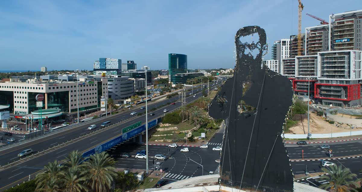 פסל הדמות של הרצליה. מחלף הסירה הרצליה על רקע אזור התעשייה ובנייני הרצליה הילס