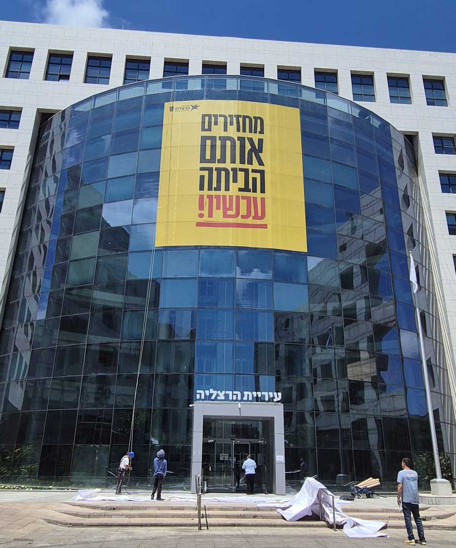באנר ענק בחזית בניין עיריית הרצליה: מחזירים אותם הביתה עכשיו