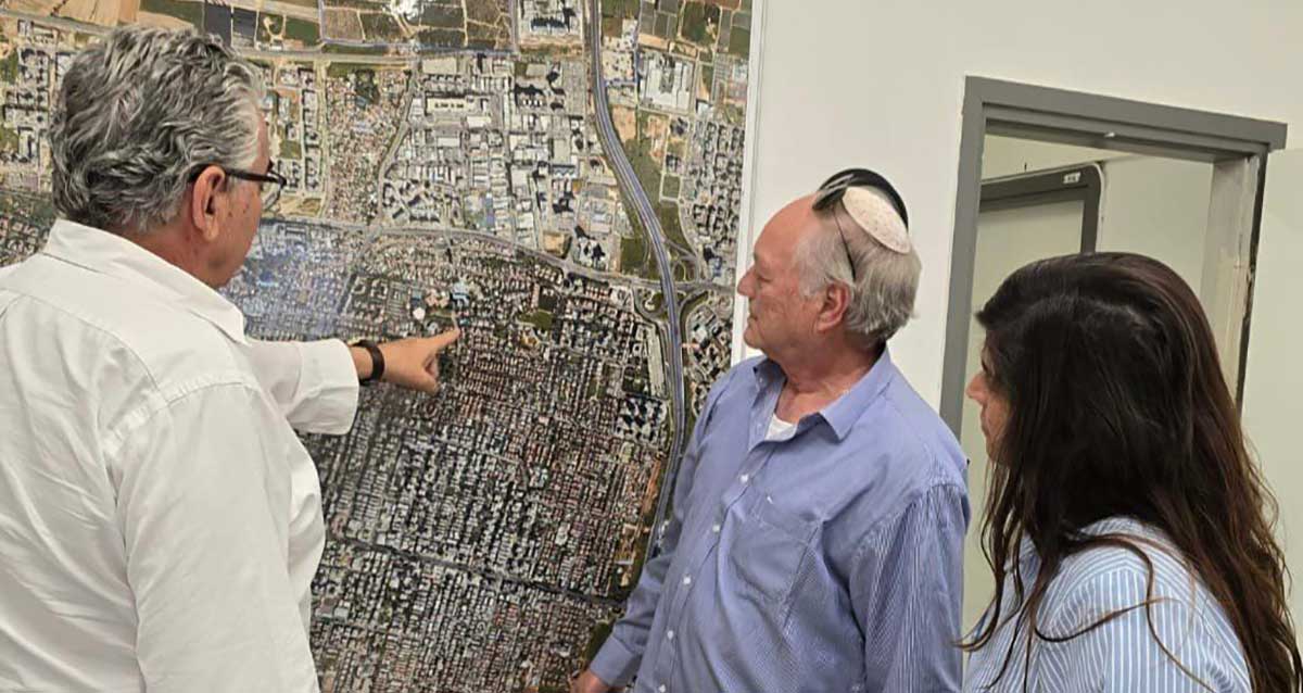 ראש העיר רעננה חיים ברוידא מצביע על מפת ענק של העיר רעננה התלויה על קיר, מביטים חבר מועצת העיר חיים גולדמן עם חברה נוספת ברקע