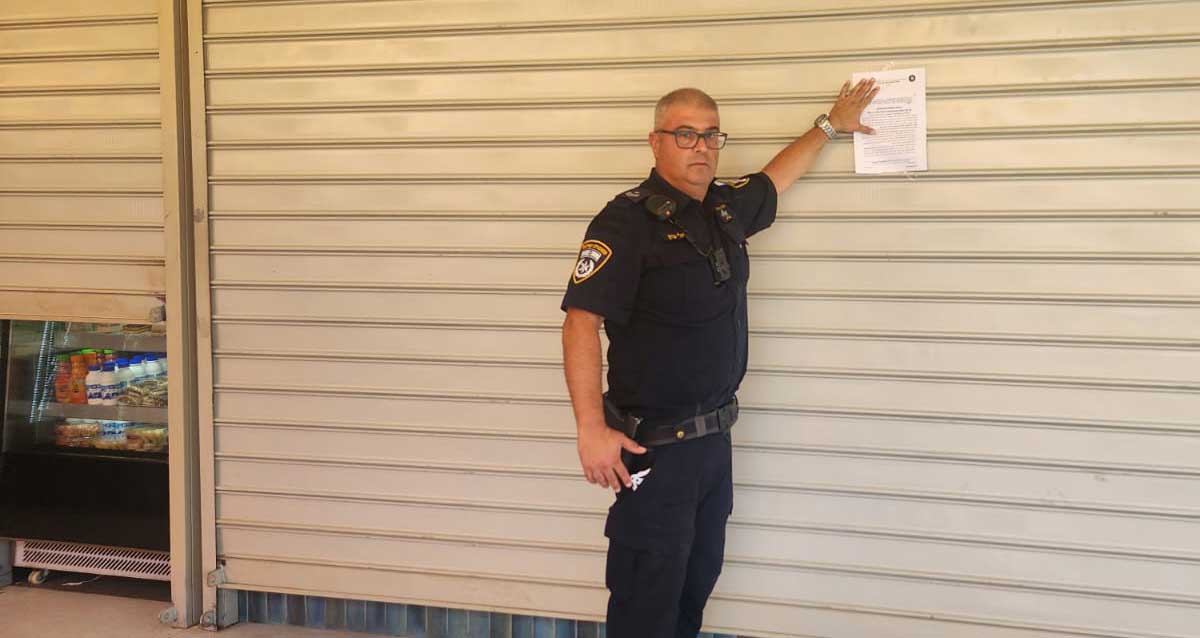 שוטר מדביק צו סגירה על דלת מאפייה בהרצליה