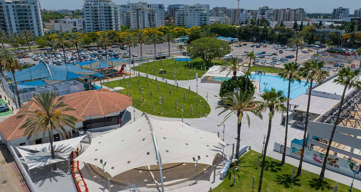 מבט על הקאנטרי של הרצליה, המבנים של הקאנטרי, בריכת השחייה, שטחים עם דשא, עצי דקל בשטח הקאנטרי, מגרשי חנייה למכוניות בסמוך לקאנטרי, וברקע בניינים גבוהים של הרצליה