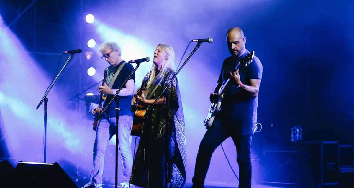 דנה ברגר בפארק הרצליה באירוע סיום בפארק הרצליה, עומדת ושרה מול מיקרופון, מנגנת בגיטרה, ולבושה בשמלה שחורה, שיער ארוך בהיר גולש. ולידה ברי סחרוף ועוד נגן מלווה שניהם עם גיטרות