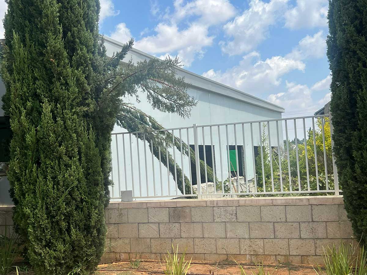 המבנה המיועד להריסה - מבט מבחוץ מבעד לגדר המתכת הניצבת על גדר אבן