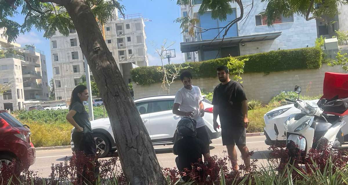 תאונת דרכים בכניסה לשכונת גליל ים שני גברים מסייעים לרוכב האופנוע שיושב עם גבו למצלמה ואשה משקיפה