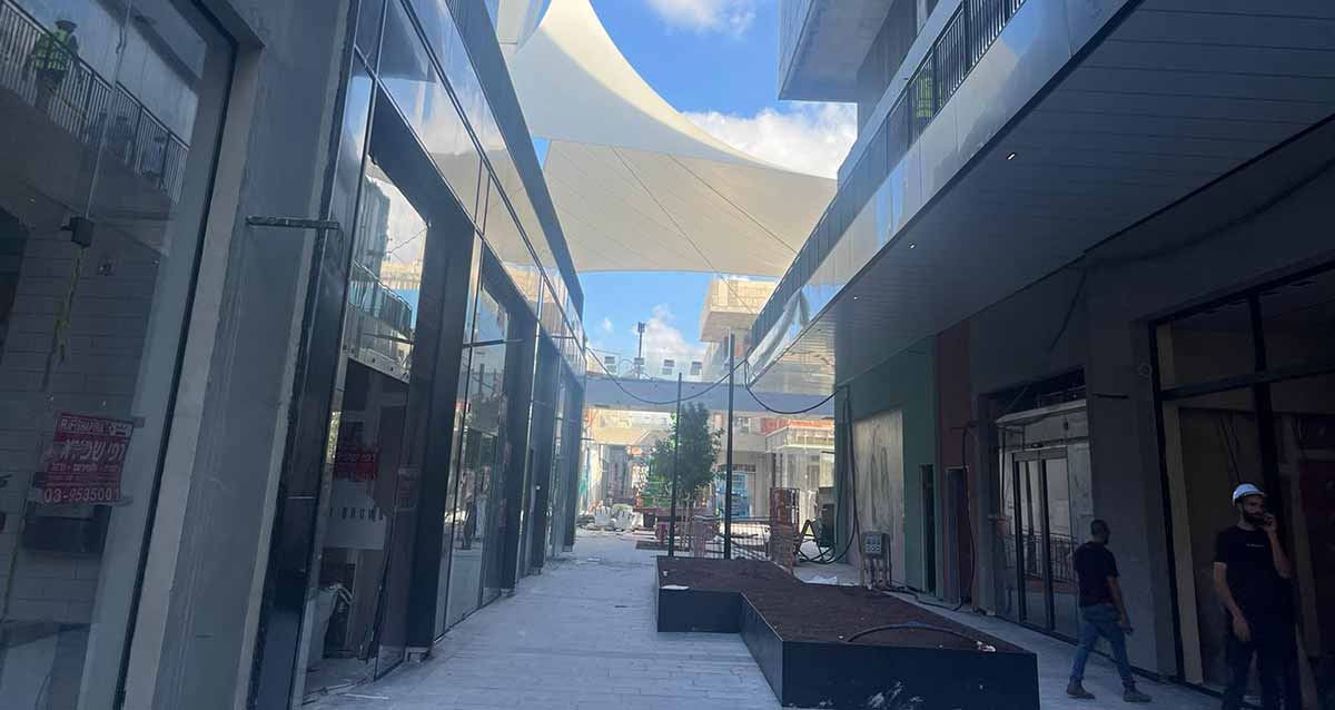 אתר קניון ביג גלילות. תמונה של רחבה בין שני בניינים בשלבי בנייה. באמצע הרחבה משטח שחור לישיבה וצורתה האות Z. מספר פועלים ברחבה.