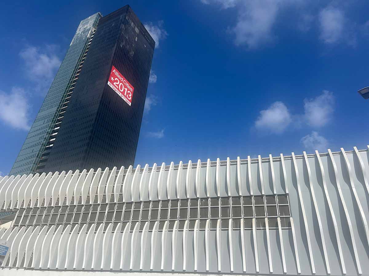 ביג גלילות רמת השרון, מגדל שחור גבוה של משרדים ושלט אדום של Allied Cities מספר טלפון 2013* וכיתוב: משרדים להשכרה. לפני המגדל בניין לכל רוחב התמונה מצופה בלוחות אנכיים ובאמצע ביניהם שורת חלונות זכוכית