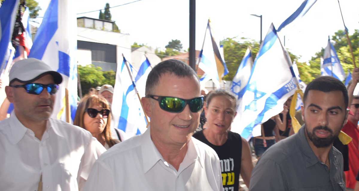 יולי אדלשטיין מלווה במאבטחים צועד בשבת מלווה על ידי מפגינים עם דגלי ישראל. צעדת הבושה