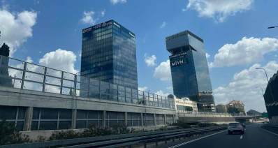 בנייני משרדים בכביש 531, שני מגדלים מצופים בלוחות זכוכית כחולה. על הבניין הימני כתוב: MIVN משרדים להשכרה ועל השמאלי כתוב: מניבים ומספר טלפון. לפני הבניינים מבנה חד קומתי עם חלונות זכוכית ובגג מעקה זכוכית. בצד ימין הכביש ומכוניות