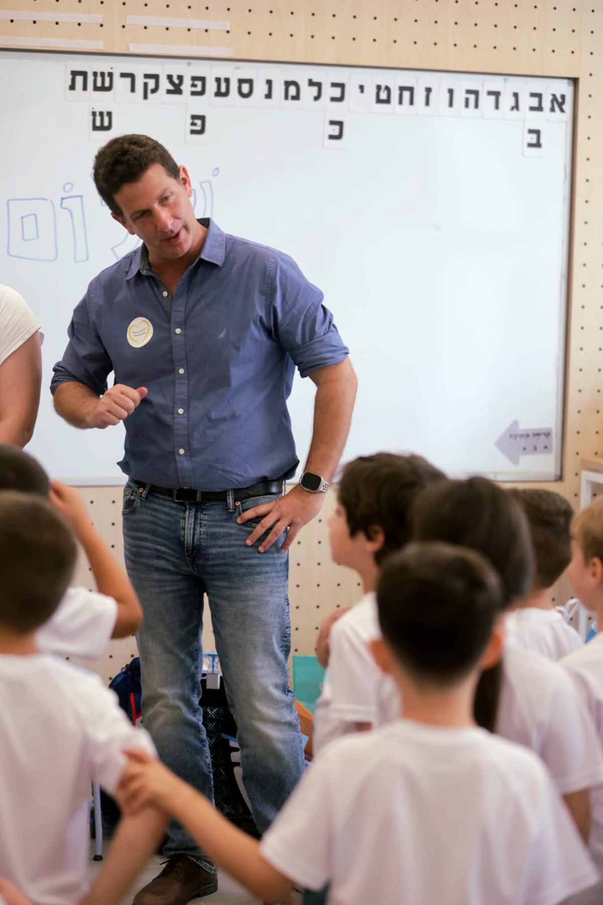 יריב פישר ראש העיר בפתיחת שנת הלימודים, עומד לפני הלוח בכיתה ומשוחח עם תלמידות ותלמידים.