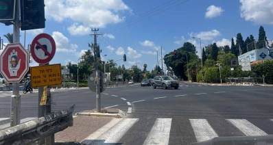 צומת רעננה כפר סבא, רמזורים בכל הצדדים, עצים לאורך הרחוב ומכוניות חוצות את הצומת.