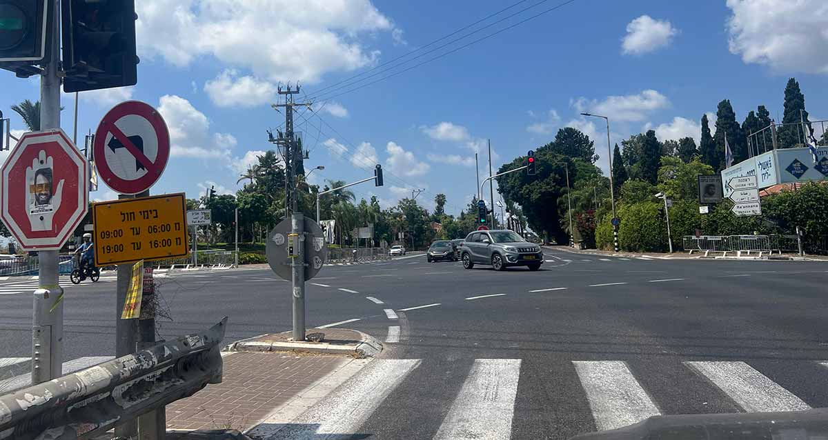 צומת רעננה כפר סבא, רמזורים בכל הצדדים, עצים לאורך הרחוב ומכוניות חוצות את הצומת.