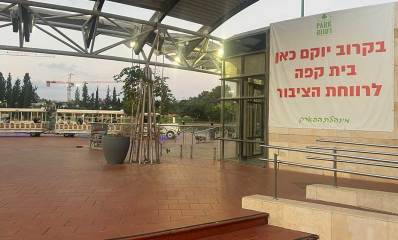 צילום של פארק רעננה עם רכבת הפארק מסיעה אנשים ומנוף ברקע. שלט ענק על הקיר של בית הקפה עם הכיתוב: prark רעננה. בקרוב יוקם כאן בית קפה לרווחת הציבור. מינהלת הפארק
