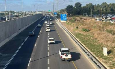 נתיבי איילון, חומת בטון גבוהה מפרידה בין שני המסלולים בקטע הכביש. שלושה נתיבים במסלול. בצד שמאל של המסלול עמודי חשמל של מסילת הרכבת בין שני המסלולים. לצד חומת הבטון נתיב אסור לתנועה. בצד ימין שדה ולידו מגרש חנייה לכלי רכב. ברקע חורשת עצים.