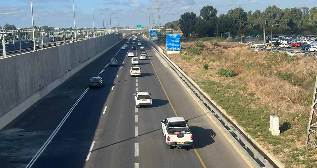 נתיבי איילון, חומת בטון גבוהה מפרידה בין שני המסלולים בקטע הכביש. שלושה נתיבים במסלול. בצד שמאל של המסלול עמודי חשמל של מסילת הרכבת בין שני המסלולים. לצד חומת הבטון נתיב אסור לתנועה. בצד ימין שדה ולידו מגרש חנייה לכלי רכב. ברקע חורשת עצים.