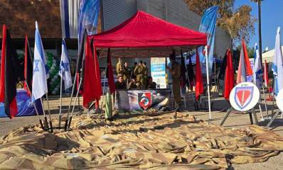 הפנינג גיוס ברמת השרון. אוהל אדום, רשת הסוואה על המשטח, דגלי המדינה ודגלי יחידות משני צידי האוהל. בתוך האוהל חיילים יושבים מאחורי שולחן שבחזיתו סמל של יחידה.