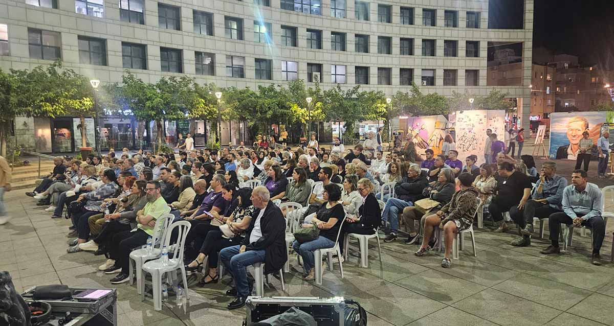מציינים בהרצליה שנה למלחמה. קהל יושב על כסאות פלסטיק לבנים בטקס ברחבת העירייה.