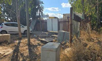 חורשת הנ"מ בהרצליה. ברקע גדר של מתחם סגור ושער לבן. מכונית לבנה ליד השער. בצד ימין זרוקים ארונות. בצד שמאל שתי מכוניות נוספות.