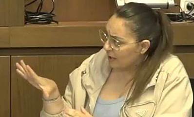 פרח מלך מנכ"לית עיריית רמת השרון. תמונה של פלג גוף עליון. יושבת במשרד ומסתכלת ימינה עם יד ימין מושטת קדימה. מרכיבה משקפי ראייה ולובשת ז'קט בז'.