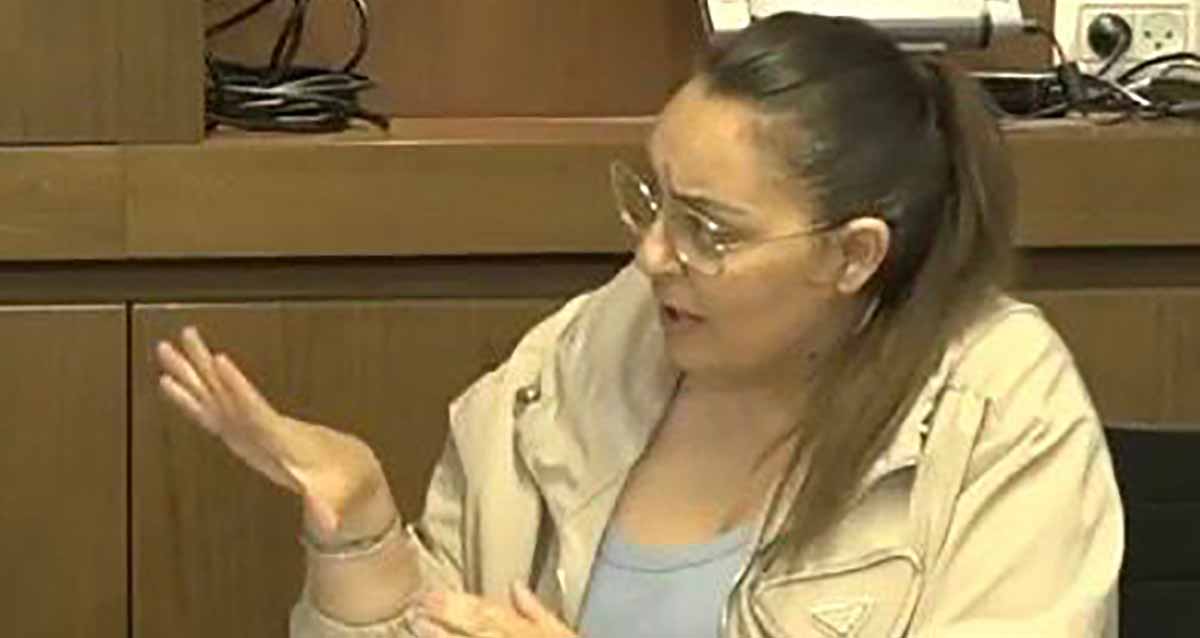 פרח מלך מנכ"לית עיריית רמת השרון. תמונה של פלג גוף עליון. יושבת במשרד ומסתכלת ימינה עם יד ימין מושטת קדימה. מרכיבה משקפי ראייה ולובשת ז'קט בז'.