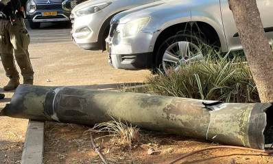 הרקטה שיורטה בשרון, מונחת על האדמה ליד מכונית בחניון של מכוניות. שני שוטרים עומדים ליד הרקטה.