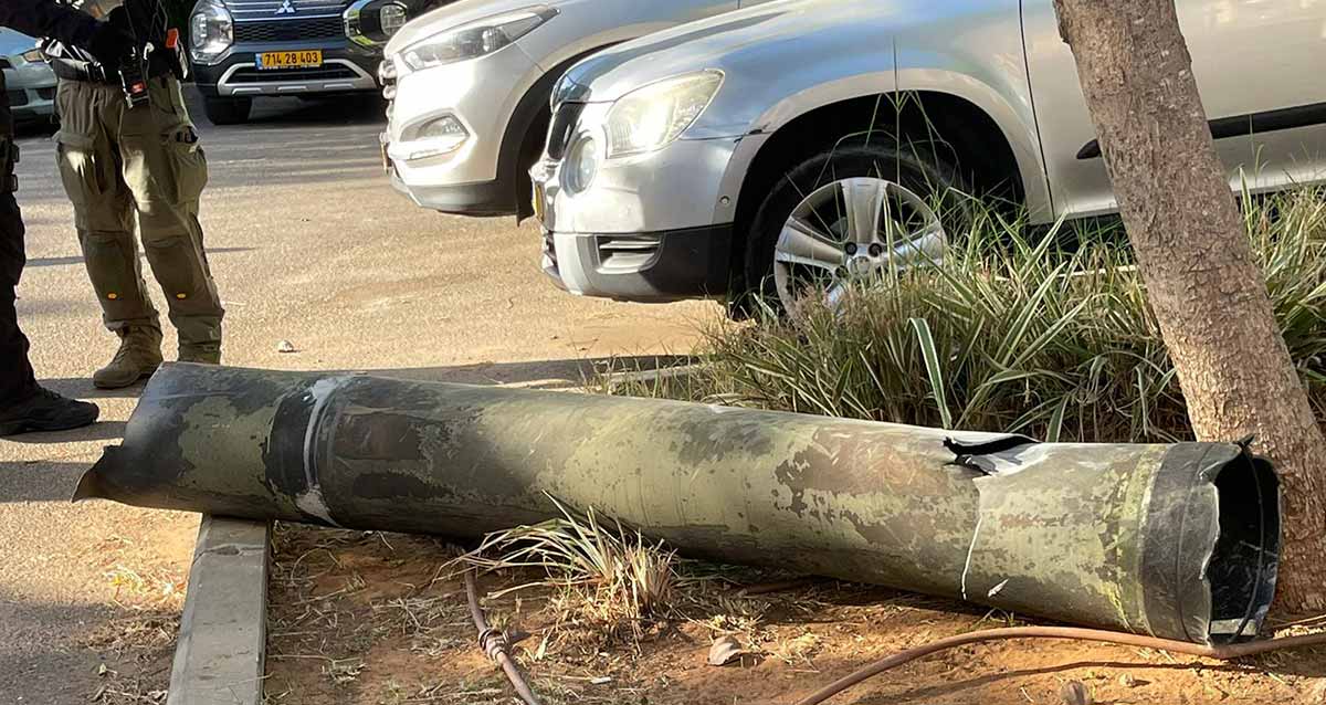 הרקטה שיורטה בשרון, מונחת על האדמה ליד מכונית בחניון של מכוניות. שני שוטרים עומדים ליד הרקטה.