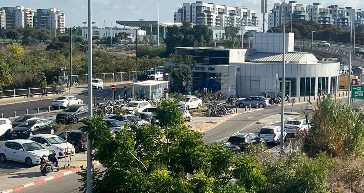 תחנת הרכבת בהרצליה. מבנה מעוגל בצידו האחורי עם חלונות זכוכית לכל הגובה. הכניסה בצד שמאל של המבנה בן קומה אחת. משמאל למבנה כבישי גישה לתחנה וחניון קטן לכלי רכב. ברקע בנייני מגורים גבוהים.
