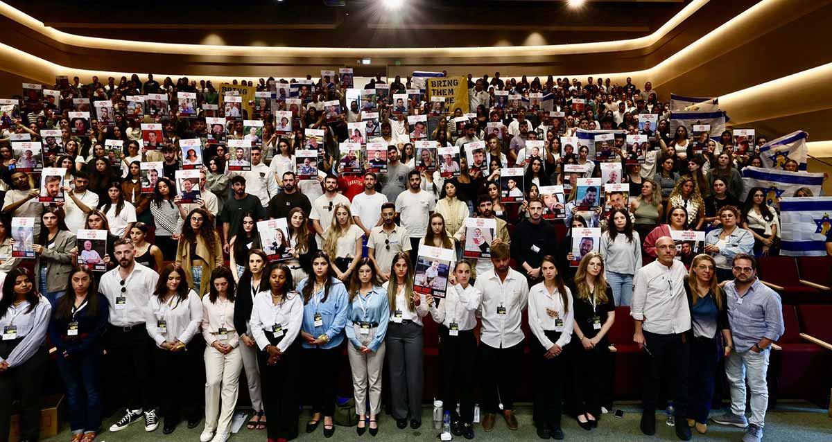 טקס פתיחת שנת הלימודים האקדמית באוניברסיטת רייכמן. סטודנטים עם תמונות של חטופים. ושלט באנגלית: BRING THEM HOME NOW