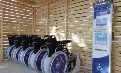 השכרת כסאות גלגלים בפארק הרצליה. סככה מקרשים בפארק הרצליה הוצבה ובתוכה חמישה כסאות. מימין לכסאות עמדת ההשכרה הממוחשבת של חברת wheelshare. מסך בעמדת ההשכרה וסמל של נכה בתחתית העמדה.