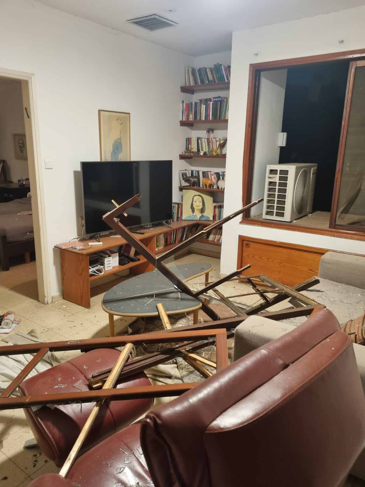 פגיעות הדף של טילים בליסטיים בסלון בית. על כורסא מעור חום זרוקים חלקי חלונות מעץ.