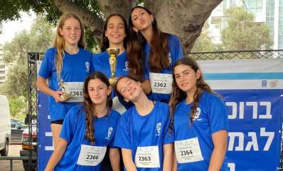 נבחרת הריצה של תלמידות עלומים. שש בנות בתלבושת ספורט ובחולצה סמל של רמת השרון. על החולצה מחובר שלט לבן עם המספר של כל אחת. אחת הבנות מחזיקה גביע.