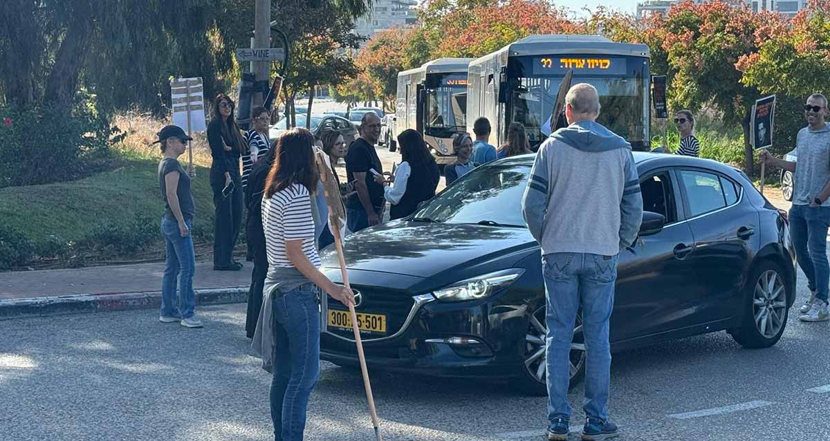 הפגנה בנחל עדה. מפגינים עומדים על הכביש וחוסמים את הכביש לתנועה.מכונית פרטית שחורה עומדת באמצע הכביש ואחריה שני אוטובוסים, ואחריהם עוד שורת מכוניות.