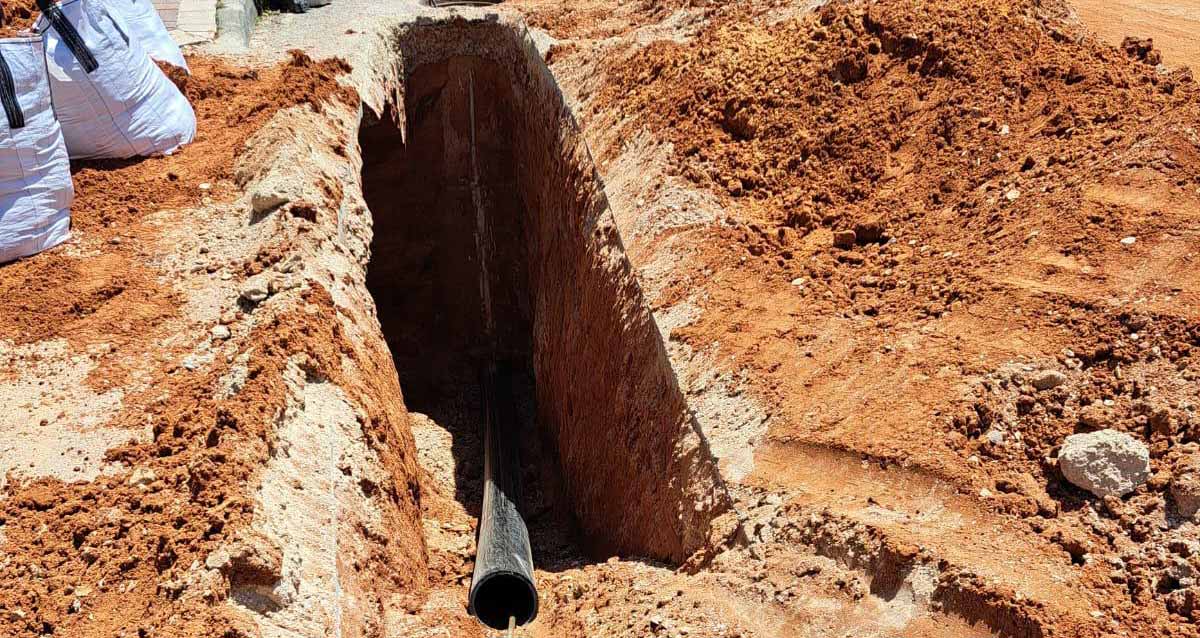 "מיה" תבצע שדרוג תשתיות הביוב בהוד השרון. חפירה עמוקה ומתוכה יוצא צינור ביוב. מימין ומשמאל לחפירה מפוזר החול שהוצא מהחפירה. בצד שמאל שקים עם חול.