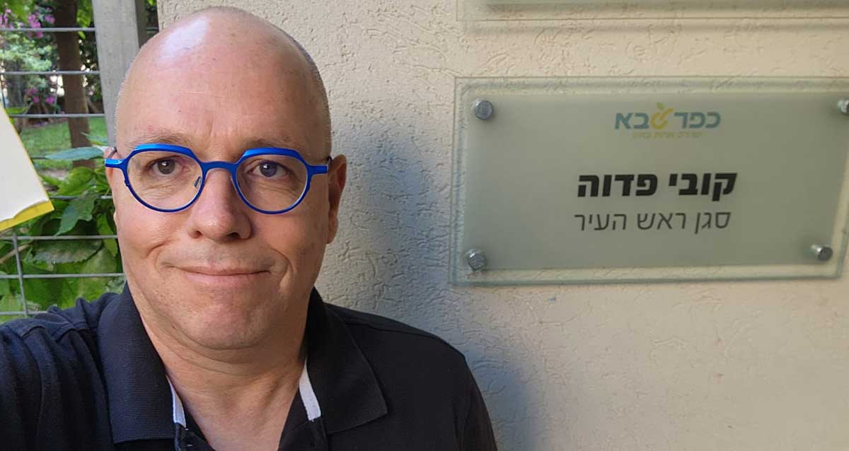 קובי פדוה ליד השלט שבו כתוב: כפר סבא. קובי פדוה סגן ראש העיר