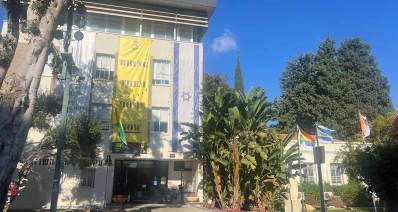 בניין עיריית רמת השרון. בניין בן 4 קומות. הכניסה בצד ימין. משמאל לכניסה על הקיר כתוב: עיריית רמת השרון. מהקומה הרביעית ועד לקומה הראשונה פרושה יריעה צהובה ועליה הכיתוב באנגלית: BRING THEM HOME NOW. מימין לשלט זה פרוש דגל המדינה באותו אורך. ומשמאל לו פרוש דגל רמת השרון. לפני הבניין עצים. מימין לבניין בחזית שלושה דגלים על תרנים. ובצד שמאל של הבניין נמצא מבנה חד קומתי ואחוריו עץ ענק.