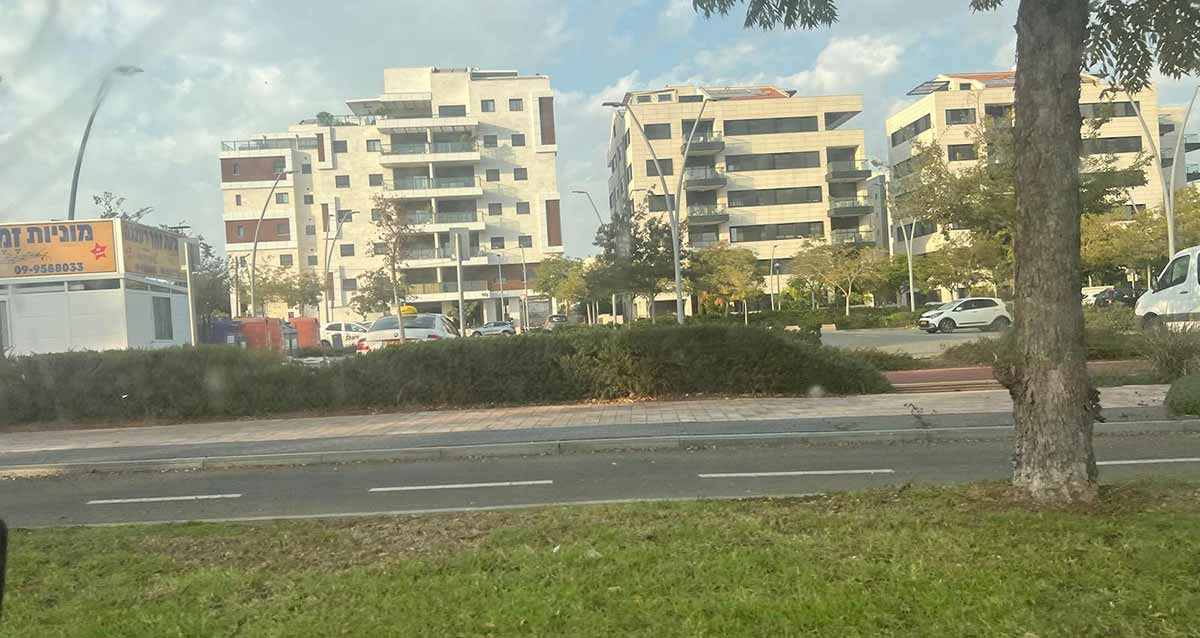 בתים בשכונת נווה זמר ברעננה, בתי מגורים בני 7 קומות. משמאל מבנה חד קומתי של תחנת מוניות. לפני הבתים מגרשי חנייה.
