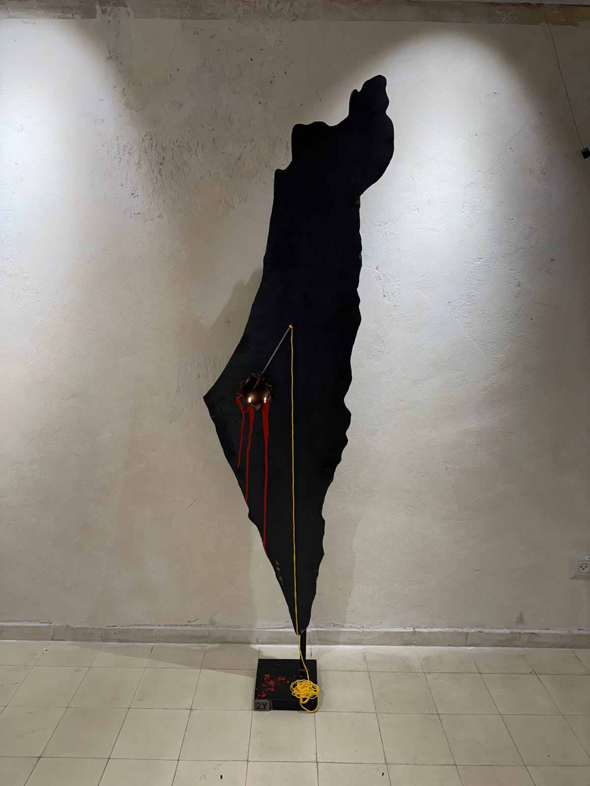 יצירה של יאיר לווינשטיין, שורד נובה. ציור של מפת מדינת ישראל מהירדן עד הים, כולה בצבע שחור.במפה מסומנות שלוש נקודות מהן יורד חבל עד הרצפה ועל הרצפה מלבן שחור עם שארית החבל.