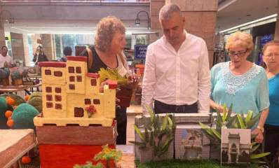 תערוכה אמנותית של ותיקי העיר כפר סבא. ראש העיר ותושבים ותיקים מתבוננים בעבודות האמנות, בתוך אולם בו העבודות מונחות על שולחנות.