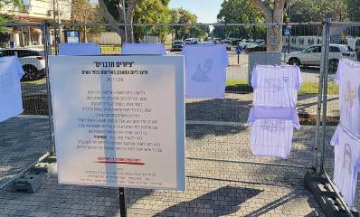 מיצג ציורים מדברים ליום המאבק באלימות כלפי נשים בתאריך 25/11/24. במרכז התמונה שלט עם הכותרת "ציורים מדברים", והסבר על המאבק והמיצג. מסביב לשלט תלויות על גדר חולצות טישרט לבנות ועליהן ציורים.