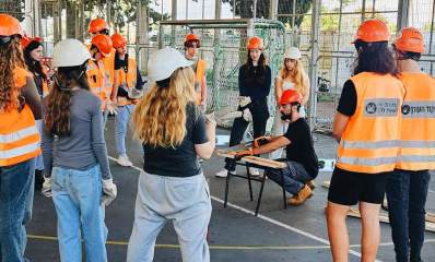מחלצים צעירים בתיכון חדש. תלמידות ותלמידים עם ווסטים וקסדות של פיקוד העורף עומדים סביב מדריך האוחז בידו משור וחותך פרופיל.