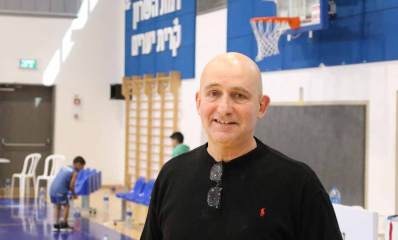 אריק דורון מנכ"ל אגודת ספורט רמת השרון. בחולצה שחורה באולם ספורט. מאחוריו סל של כדרסל. על הקיר מאחוריו כיתוב: רמת השרון קרית יערים וסולם התעמלות על הקיר מתחת לכיתוב. שני ילדים מאחוריו.