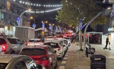 רחוב סוקולוב בהרצליה. עמוס מכוניות בשני נתיבים. רחוב חד סיטרי. מעל הרחוב תלויות מנורות בשרשרות.