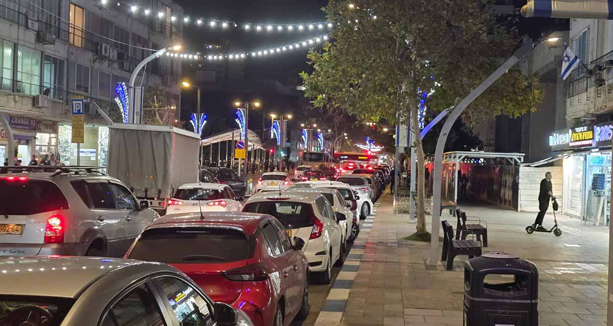 רחוב סוקולוב בהרצליה. עמוס מכוניות בשני נתיבים. רחוב חד סיטרי. מעל הרחוב תלויות מנורות בשרשרות.