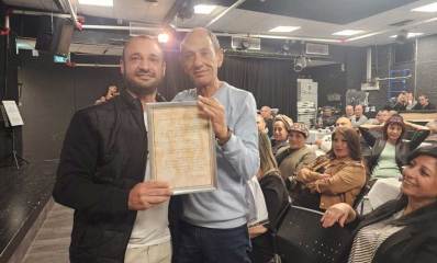 איציק כהן וליאור אהרון מחזיקים תעודה. מאחוריהם קהל עובדים ובני משפחה בטקס הפרישה של איציק אהרון