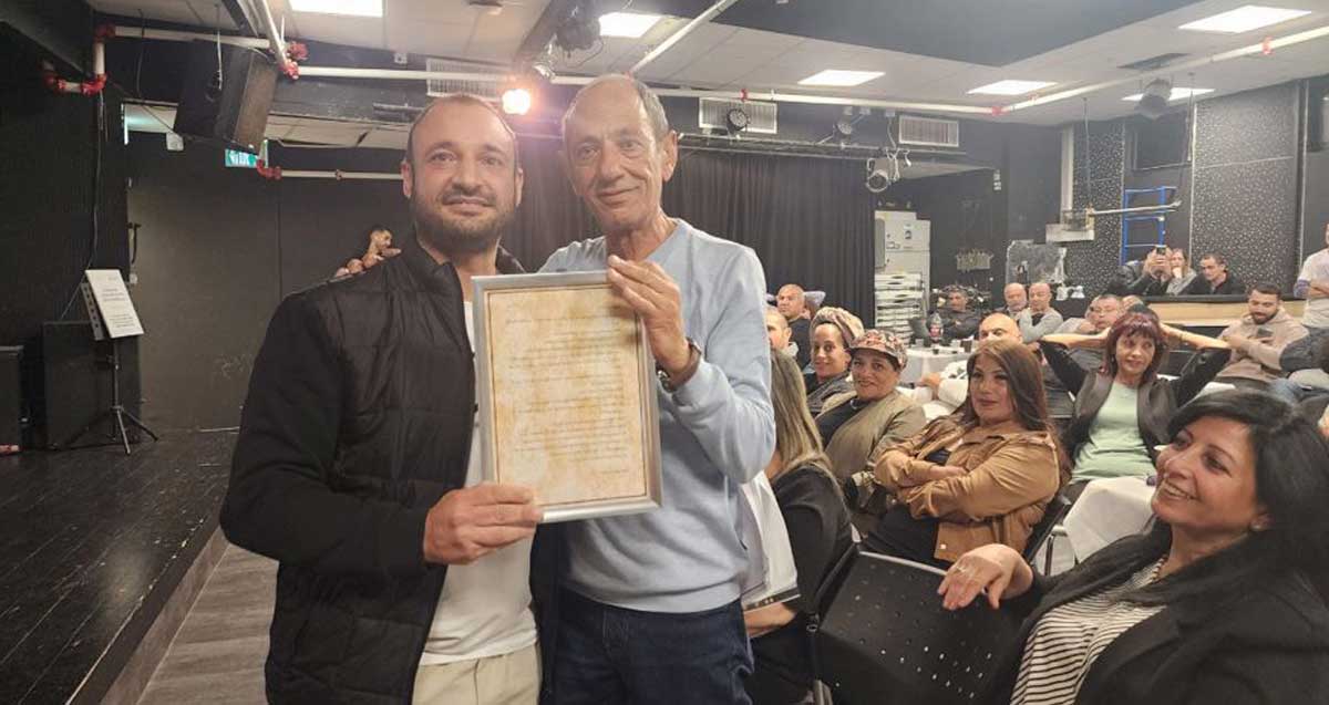 איציק כהן וליאור אהרון מחזיקים תעודה. מאחוריהם קהל עובדים ובני משפחה בטקס הפרישה של איציק אהרון