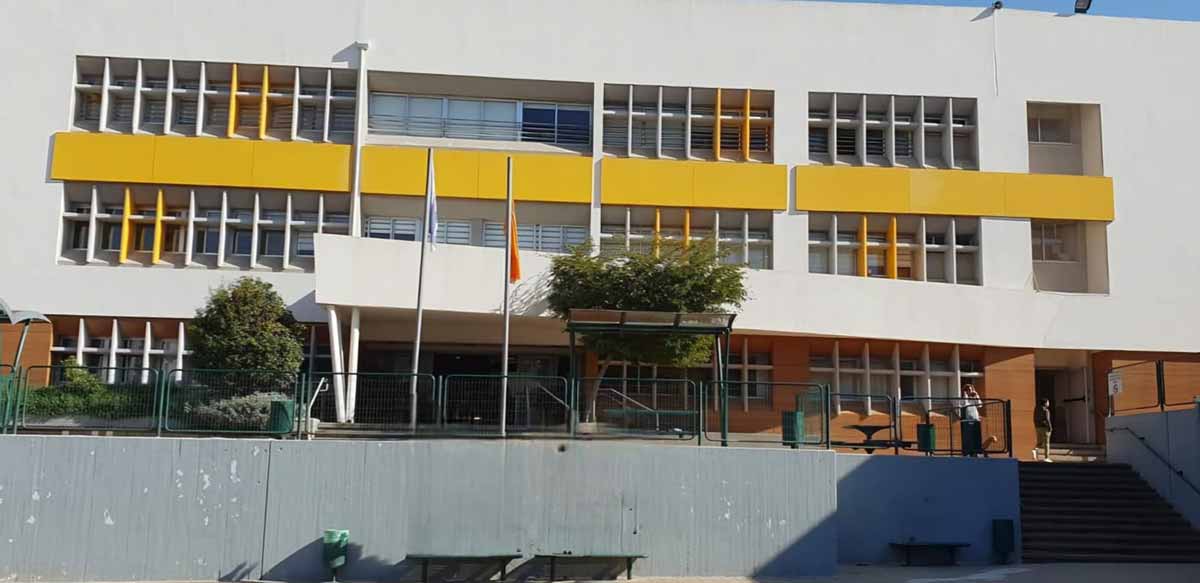 תיכון ע"ש ב. אוסטרובסקי ברעננה. תמונה מבחוץ של הבניין, בן שלוש קומות. בין קומה שתיים לשלוש פס הבטון צבוע בצהוב.