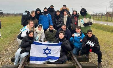 מסע תלמידי התיכונים מרמת השרון לפולין. קבוצה של כ-18 תלמידים על מסילת ברזל של הרכבת. שני תלמידים בחזית התמונה אוחזים בדגל ישראל.