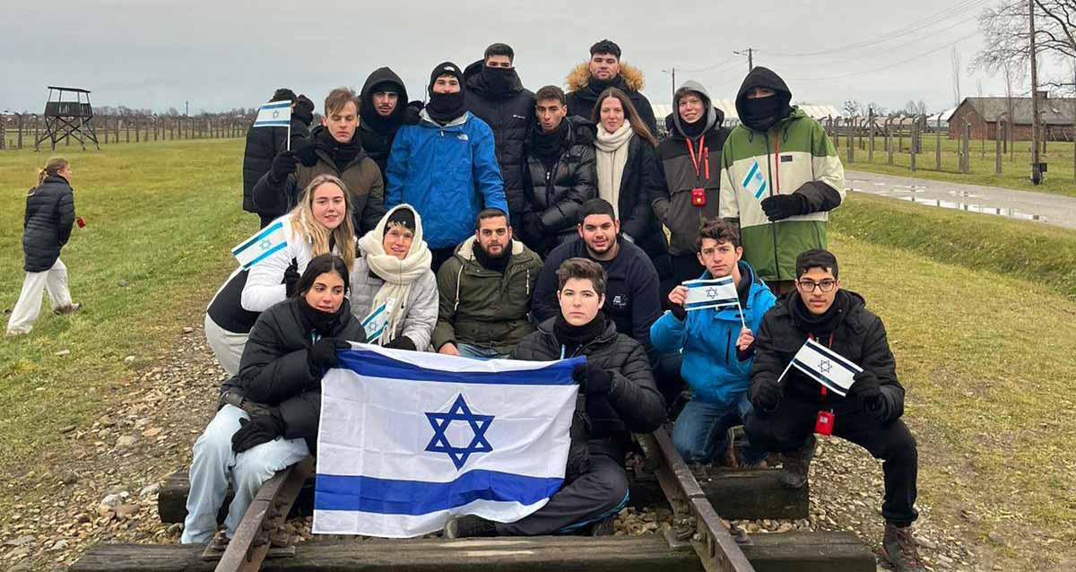 מסע תלמידי התיכונים מרמת השרון לפולין. קבוצה של כ-18 תלמידים על מסילת ברזל של הרכבת. שני תלמידים בחזית התמונה אוחזים בדגל ישראל.