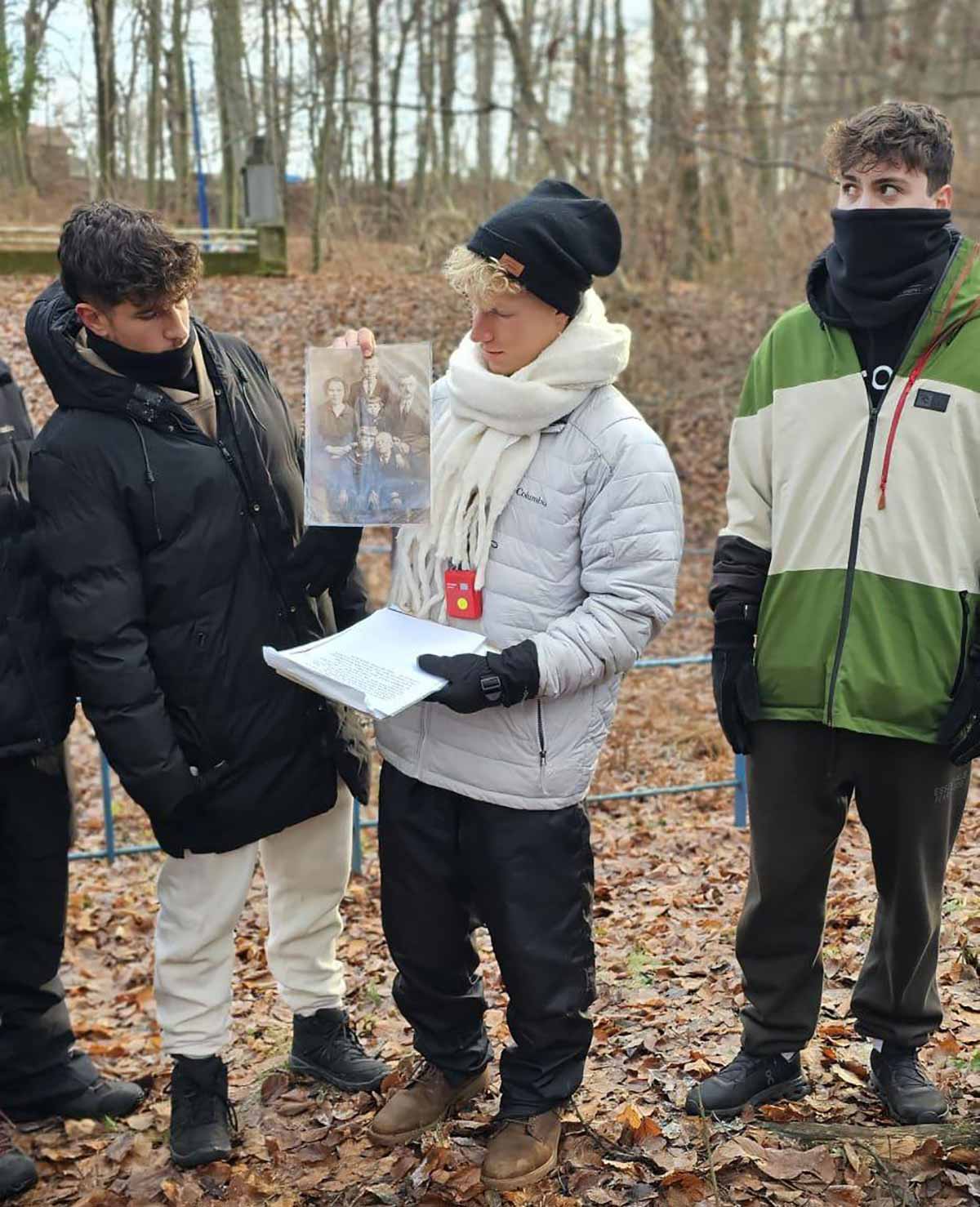 מסע תלמידי התיכונים מרמת השרון לפולין. תלמידים ומדריך עם תמונה ומכשיר אדום תלוי עליו.