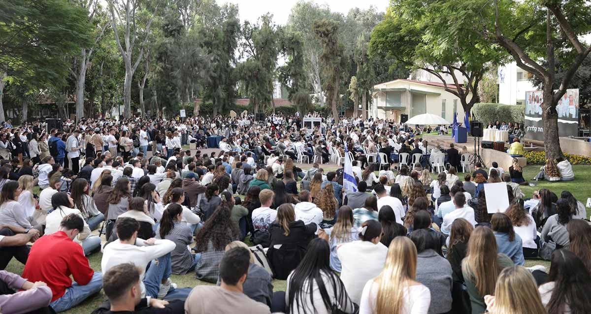 עצרת תמיכה במשפחות החטופים באוניברסיטת רייכמן. קהל הסטודנטים יושב על דשא ועל כסאות ברחבה גדולה מול הבמה של העצרת. עצים מסביב.
